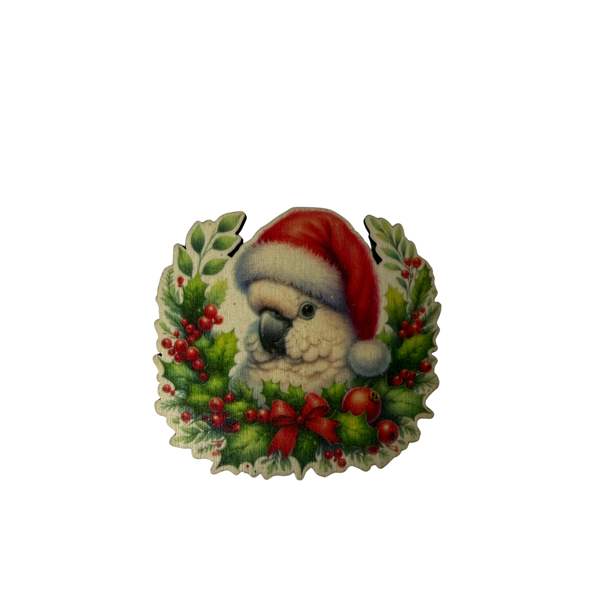 Wooden cockatoo Christmas magnet wearing a Santa hat, surrounded by green foliage, red berries and a red bow on a white background.