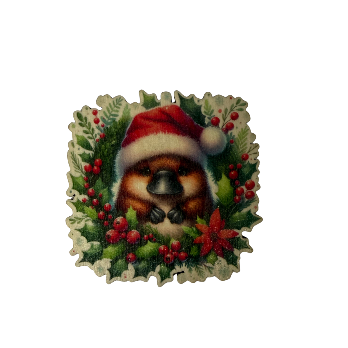 Wooden platypus Christmas magnet wearing a red Santa hat, surrounded by green foliage, red berries and a red flower on a white background.