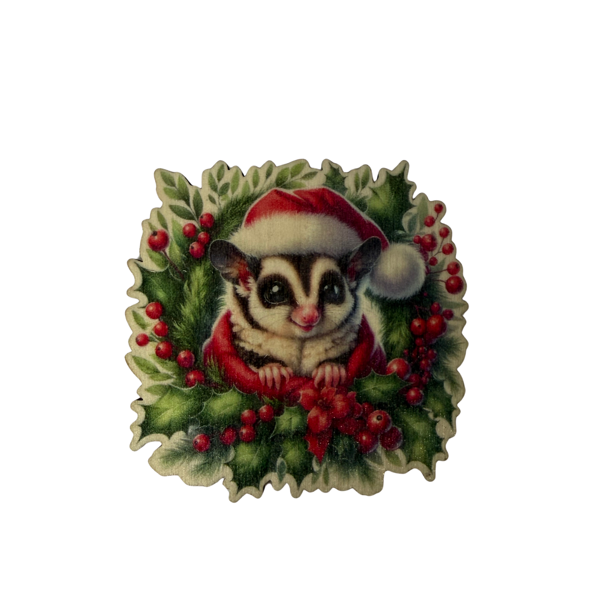 Wooden sugar glider Christmas magnet wearing a red Santa hat, surrounded by green foliage and red berries on a white background.