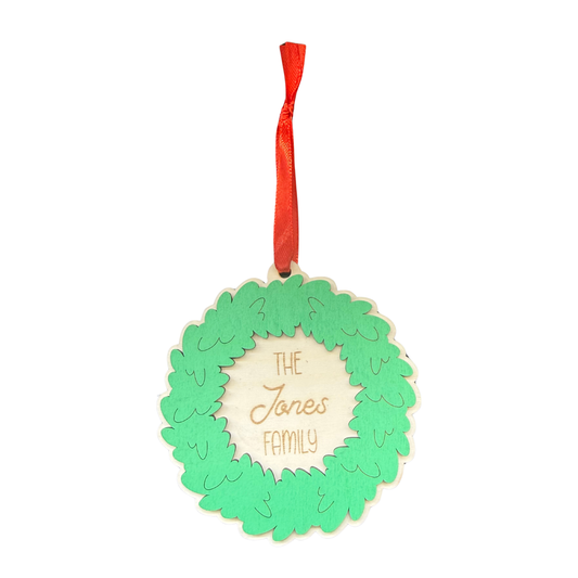 Personalised wooden Christmas wreath ornament with green leaves, Jones family engraving and red ribbon
